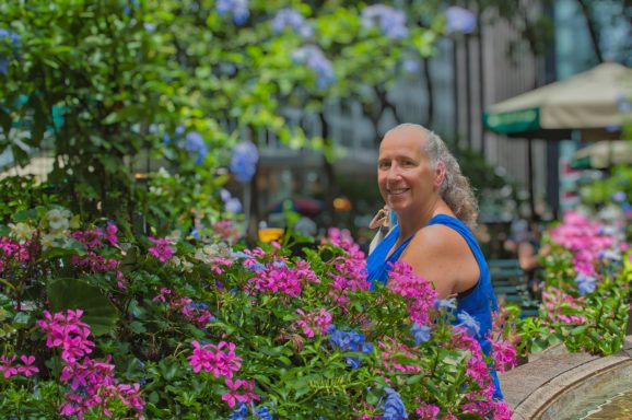 Women Posing next to flowerbed Woman with a ponytail stands among vibrant pink and purple flowers in a park setting.