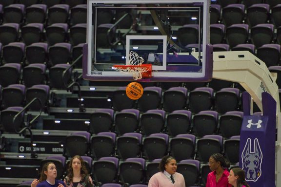 Basketball hoop with a ball just above the net, spectators in the background.
