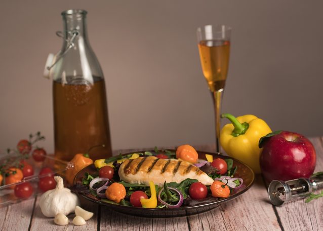 Grilled chicken with vegetables, cherry tomatoes, and a glass of beverage on a wooden table.