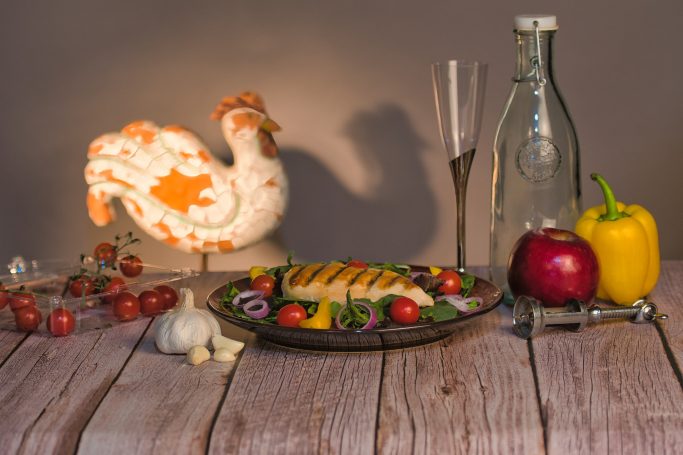 A decorative turkey, a plated dish with vegetables, and bottles on a rustic wooden table.