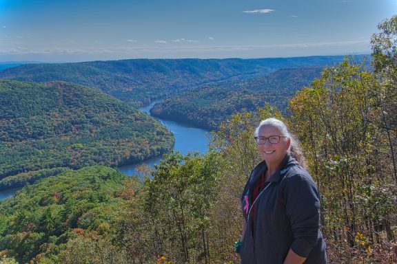 Woman standing on a ridge overlooking a winding river and lush, green hills.