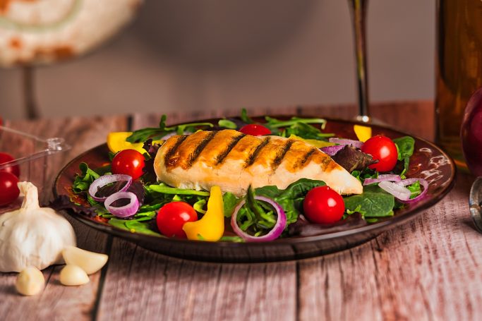 Grilled chicken breast on a bed of mixed greens, cherry tomatoes, and bell peppers.