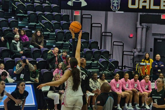 A basketball player leaps for a shot while teammates and spectators watch.