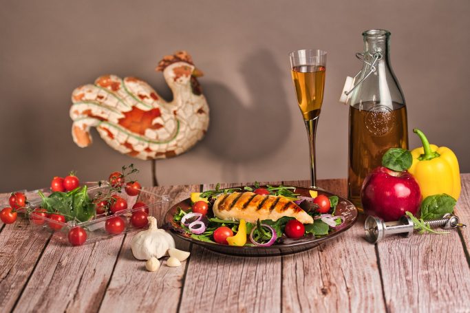 A colorful dish featuring grilled fish, fresh vegetables, and a glass of drink on a rustic table.