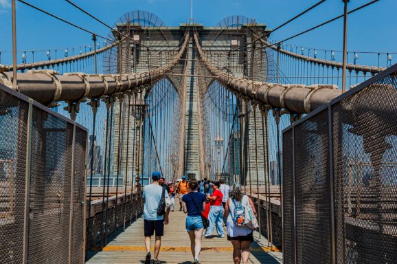 People walking across Brooklyn Bridge on a sunny day.