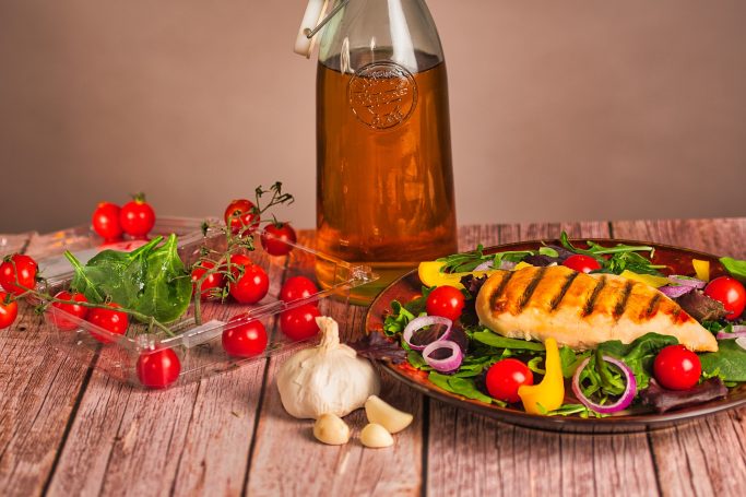 Grilled chicken on a salad with cherry tomatoes, bell peppers, and olive oil.