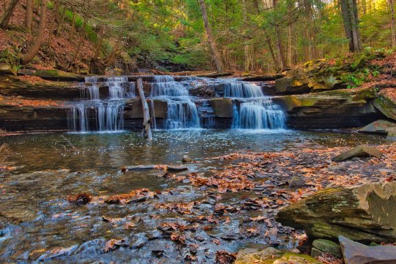 A tranquil waterfall cascading over rocks into a serene pool, surrounded by autumn foliage.