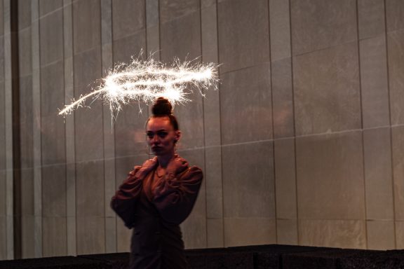 Person in a sparkly outfit poses with sparklers creating a halo effect above their head.